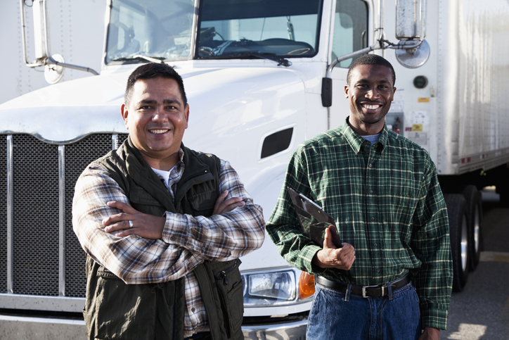 Hispanic and African American truck drivers standing in front of semi-truck.